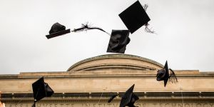 Graduation hats fly through the air against a background of gray sky and the top of the MIT dome