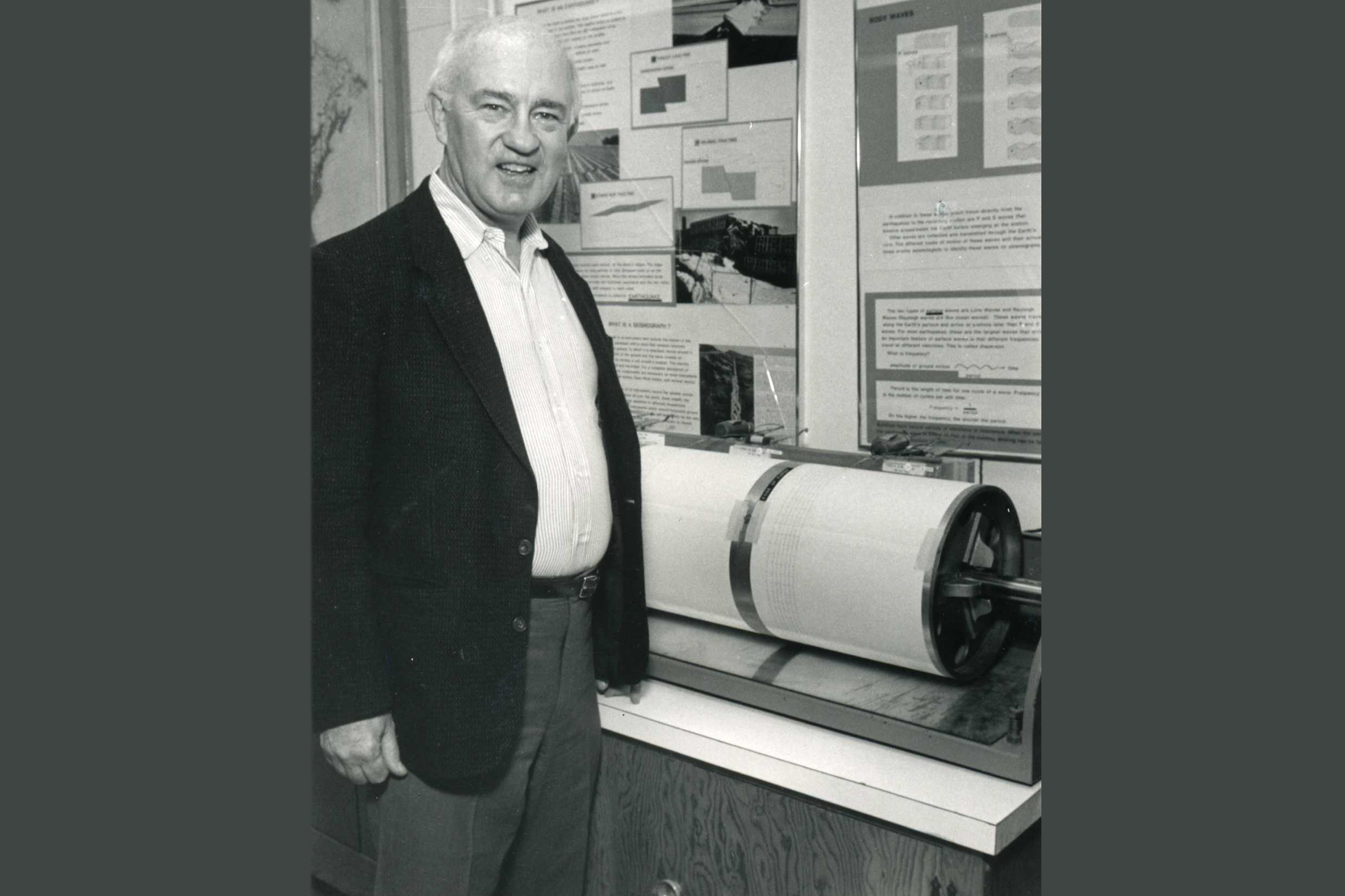A black and white photo of MIT alum Lynn Sykes standing next to a spherical piece of equipment