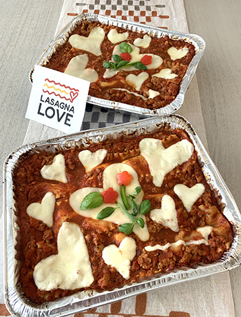 A photo showing two trays of prepared lasagna with cheese cut in the shape of hearts on the top
