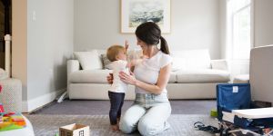 Jess Galica kneeling on a carpet with a baby on her left and a white couch behind