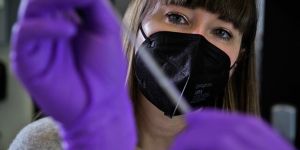 Closeup of Betar Gallant wearing a black mask and looking at a tube she holds in purple-gloved hands.