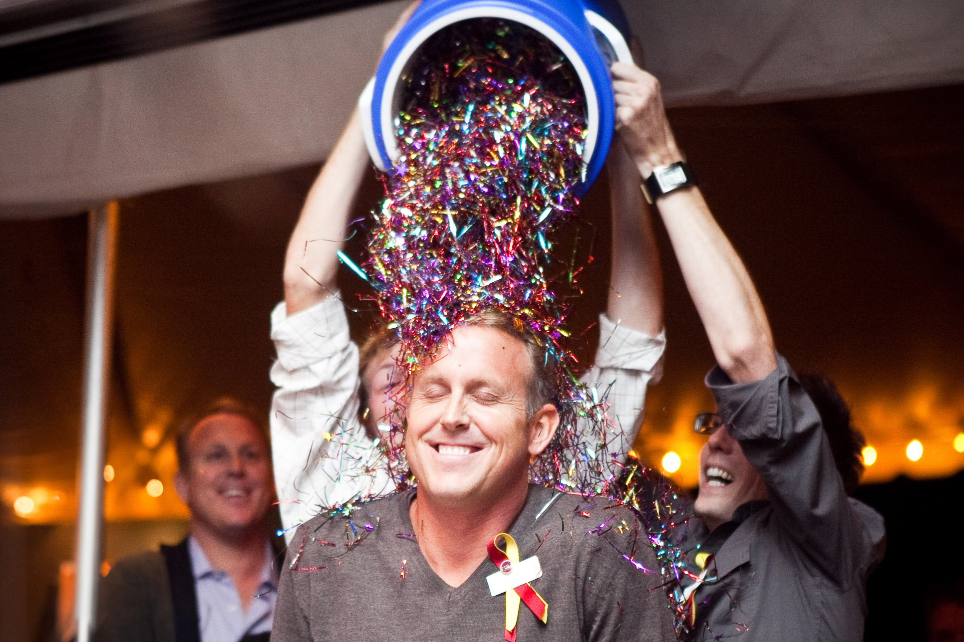 A photo of Chris Schell while two people are dumping a bucket of confetti over his head