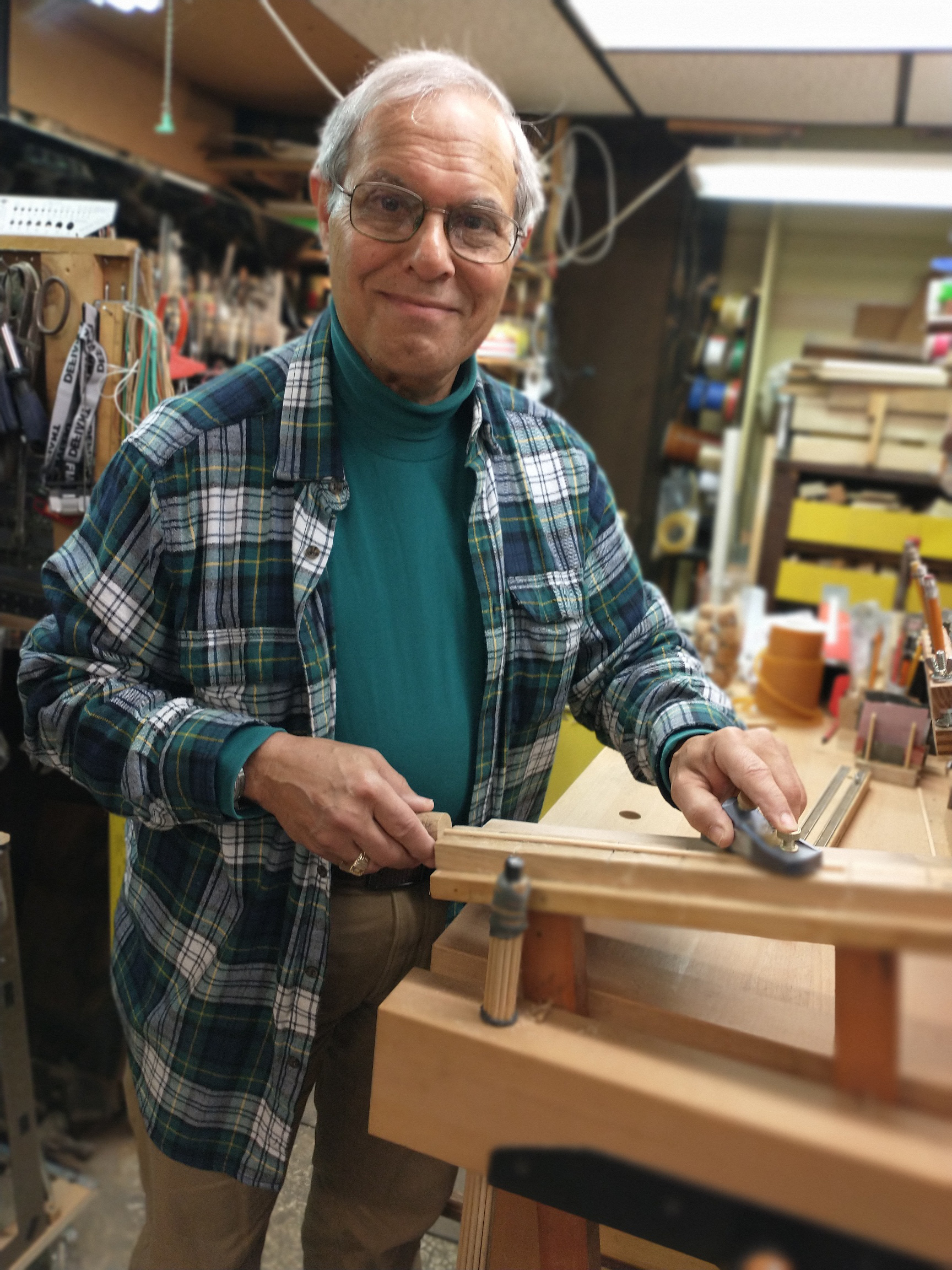 A photo of Mark Horowitz in his workshop with a wooden item in his hands leaning on a work bench