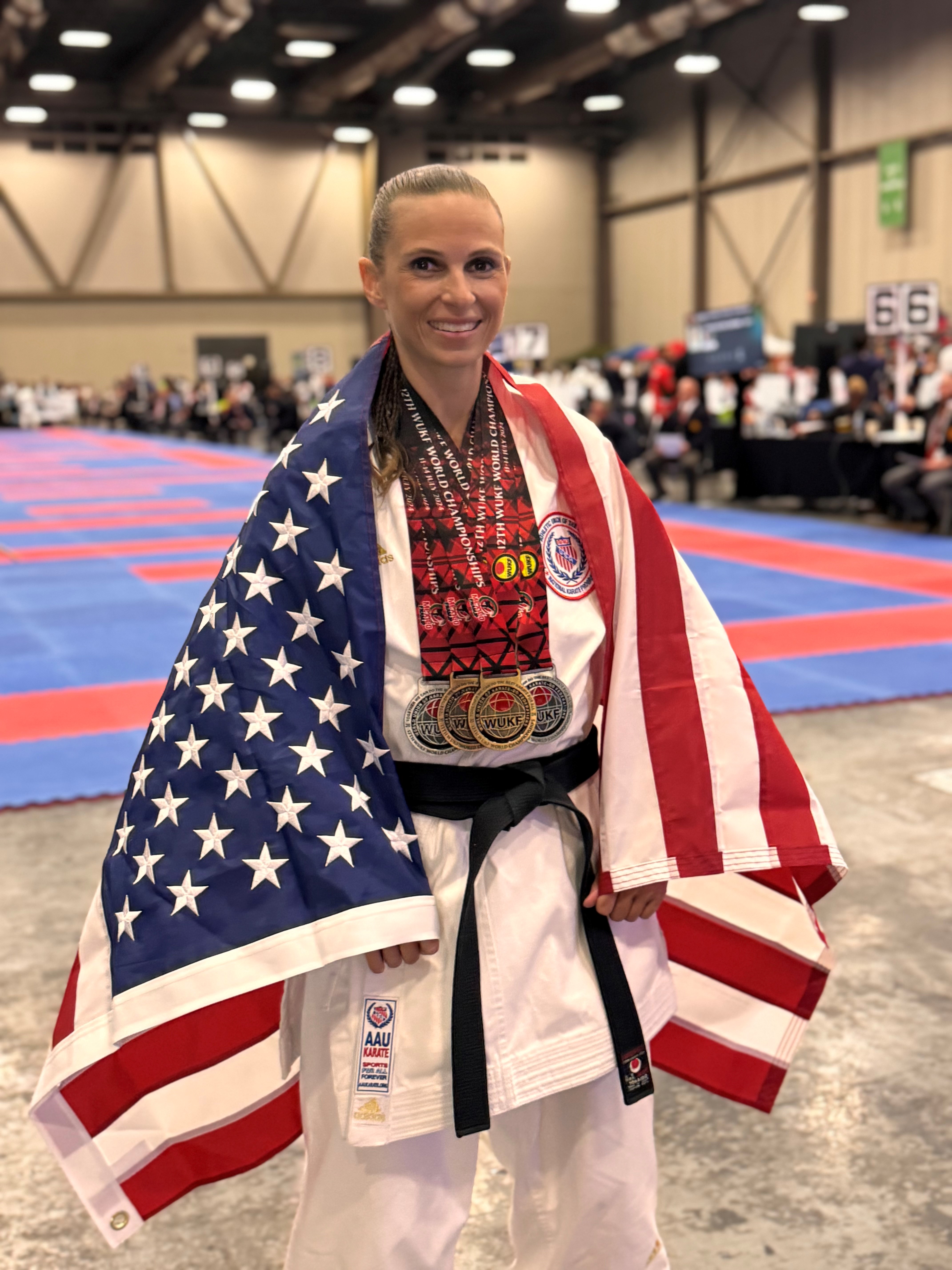 A photo of Noelle Kanaga DeLuca standing inside a building with an American flag draped over her shoulders