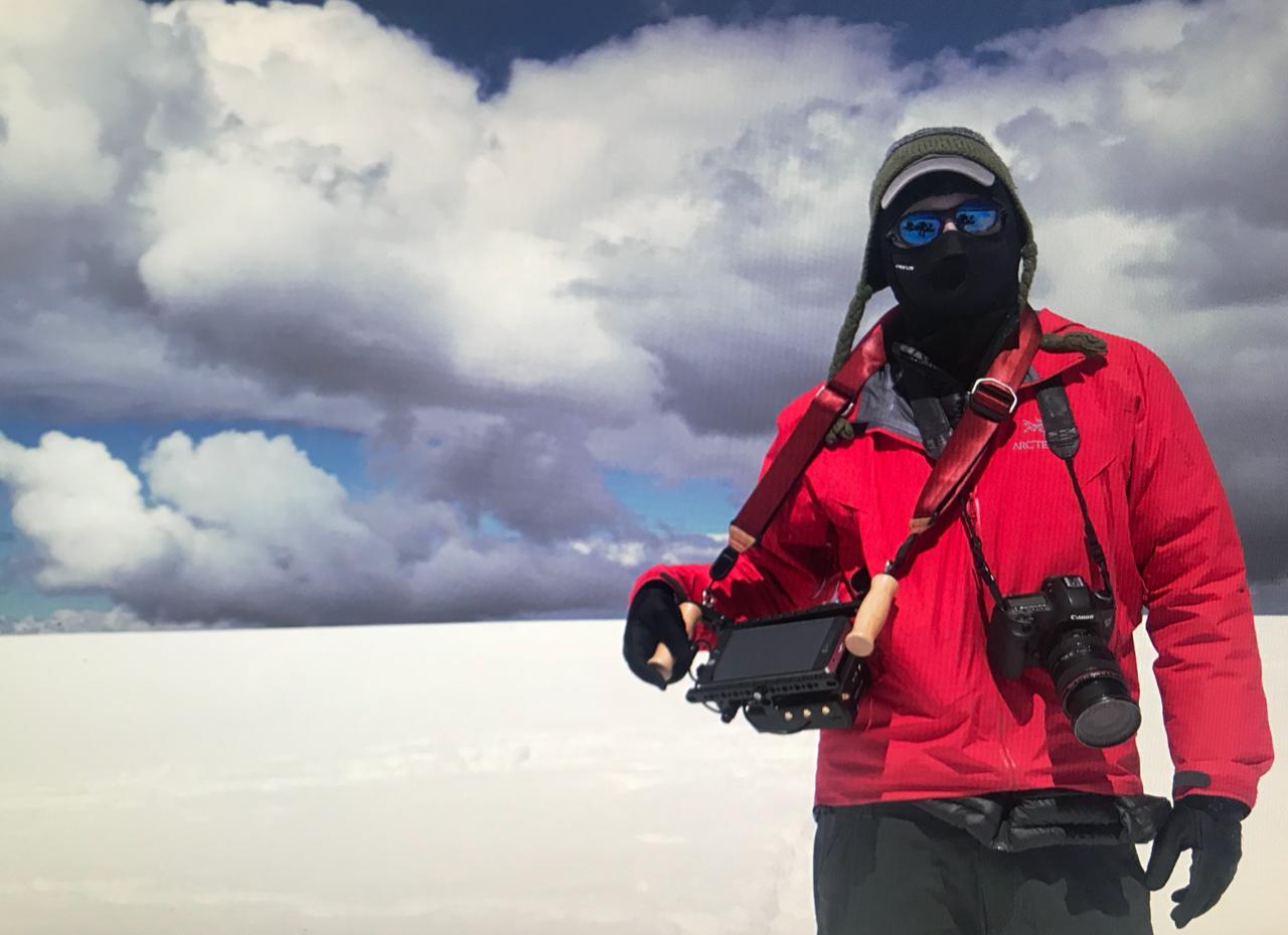 Photo of Alex Rivest outside standing in snow with clouds behind him while holding a director's monitor and wearing a ski mask
