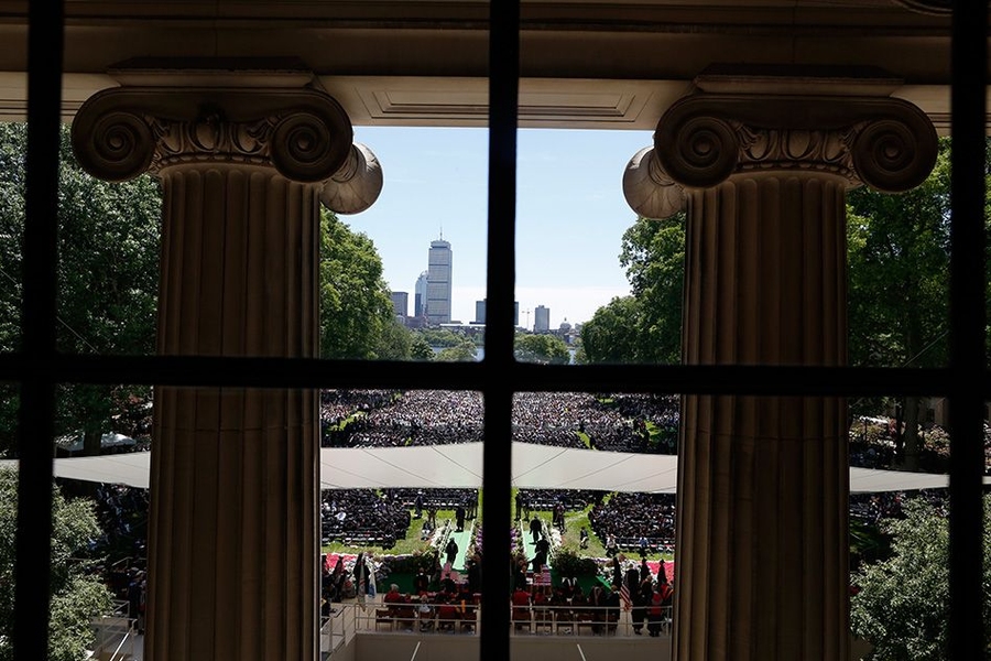 Pillars of Killian court frame a view of the commencement ceremony with the Boston skyline in the background