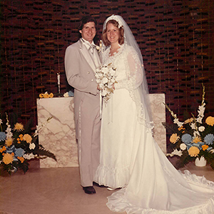 A photo of Eduardo Juncosa and Susan Juncosa in a wedding gown and suit at the alter of the MIT Chapel