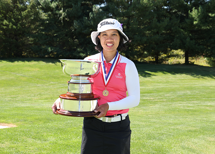 A photo of MIT alum Kimberly Dinh holding a golf tournament trophy while standing on a golf course