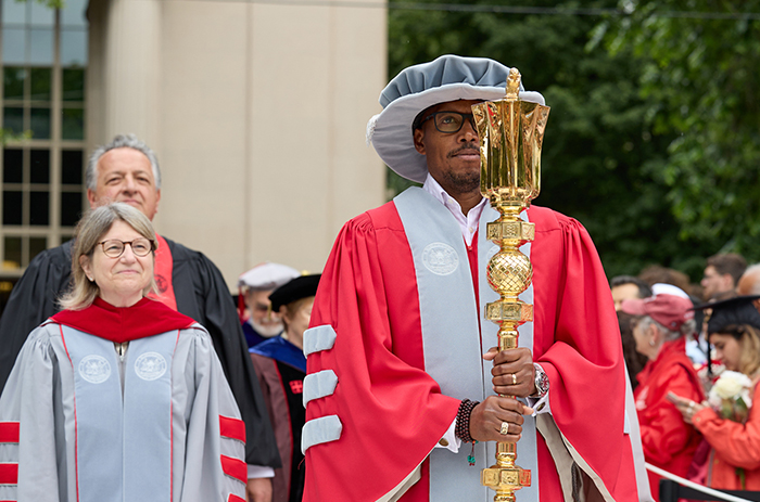 A photo of MIT alum Robert Wickham carrying a gold mase and wearing graduation robes while leading commencement with MIT president Sally Kornbluth behind him