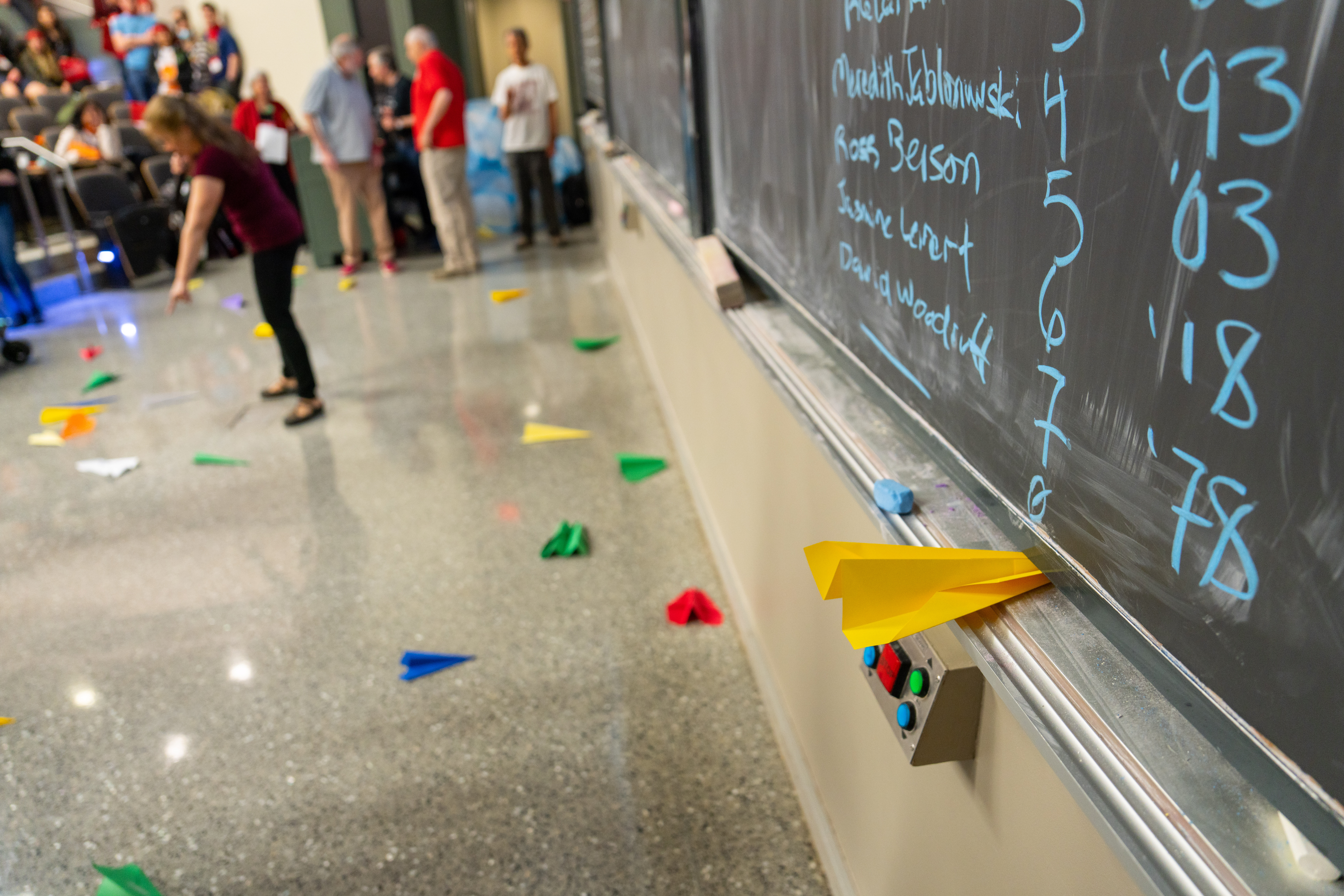 Image: close up of the scores recorded on a chalk board with paper airplane scattered across the floor in the background