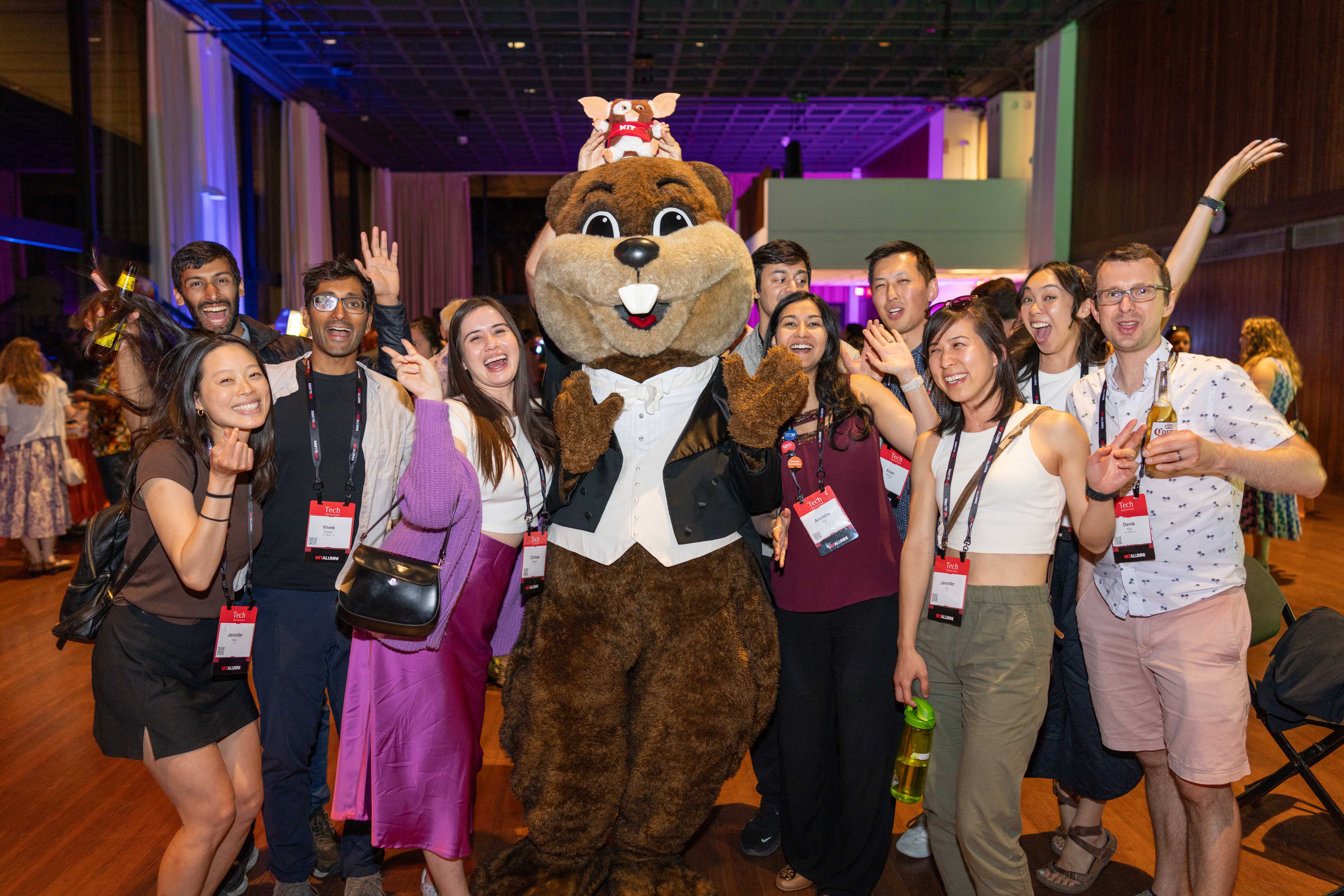 A group of young alumni pose and cheer with Tim the Beaver mascot.