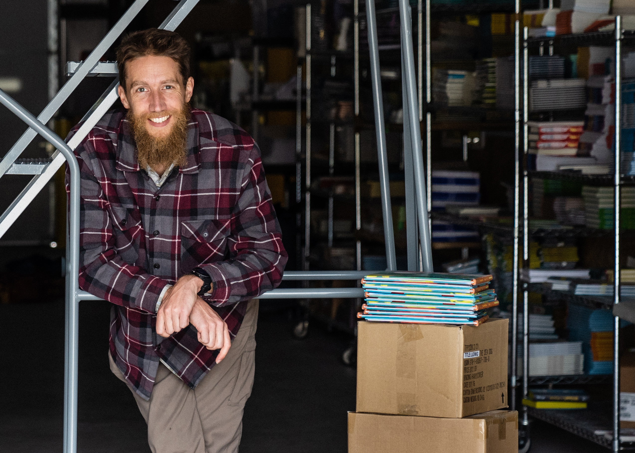 Literati CEO Charlie DeTar poses in a warehouse next to a stack of books. 