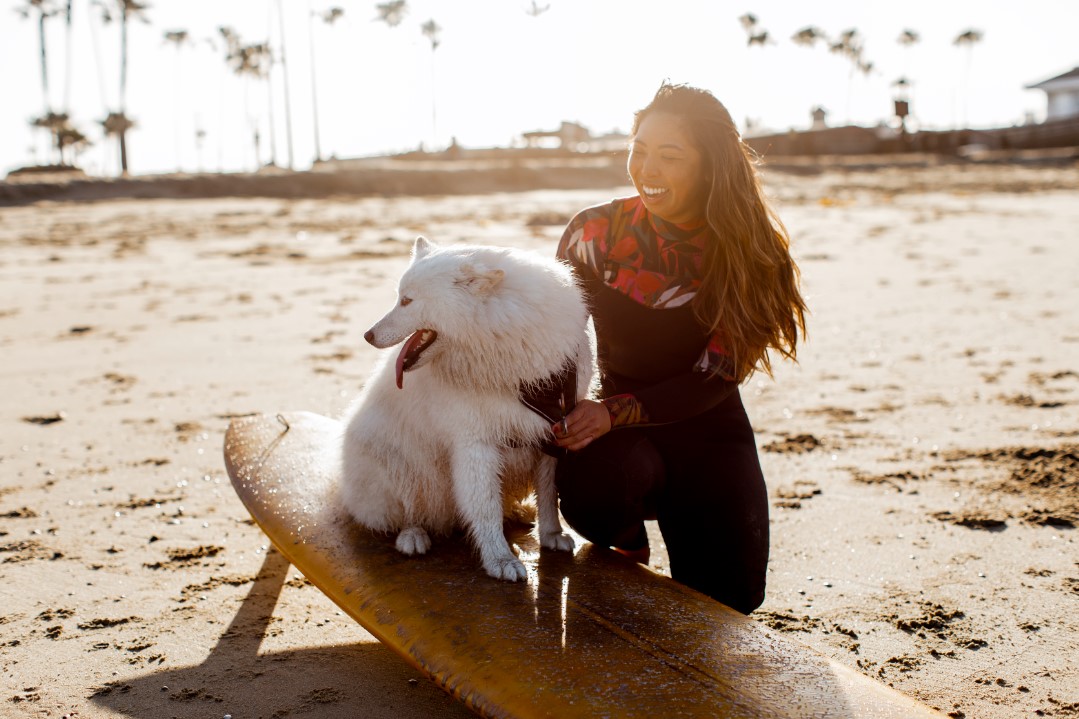 Lily Bui on a beach with her dog sitting on a surfboard