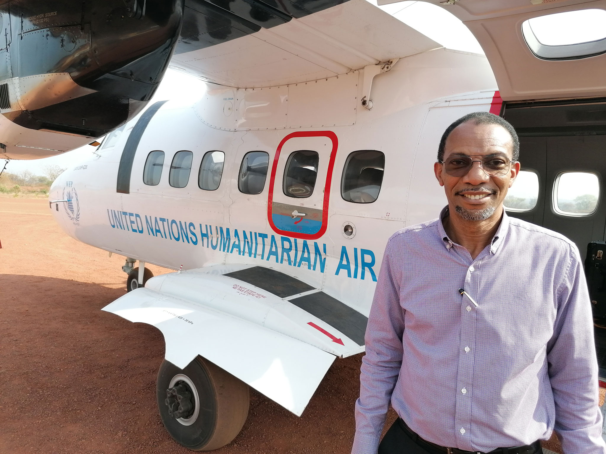 Chris Nikoi stands on a tarmac in front of a United Nations humanitarian aircraft.