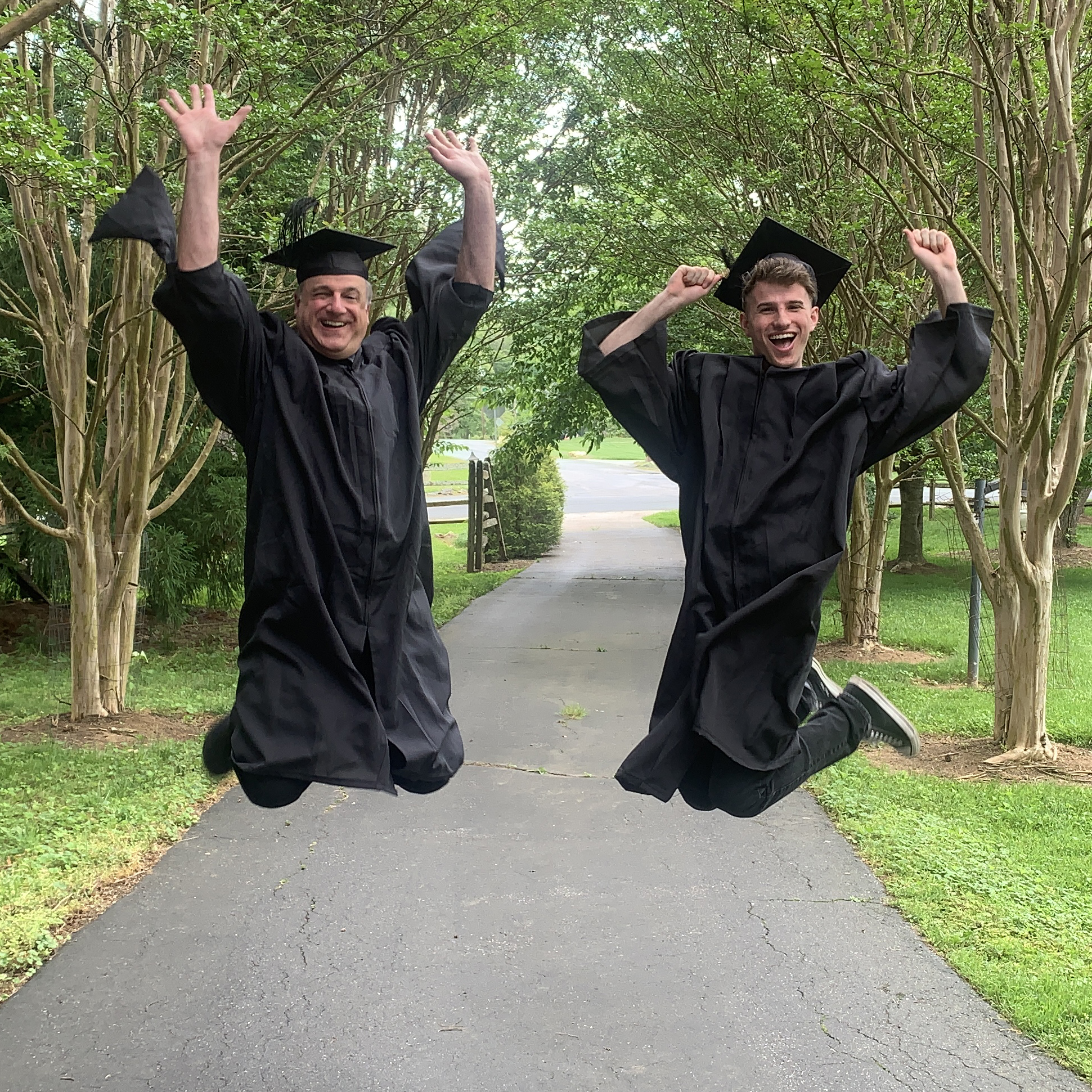 Father and son Michael and Sam Solomon leap into the air wearing their graduation gowns