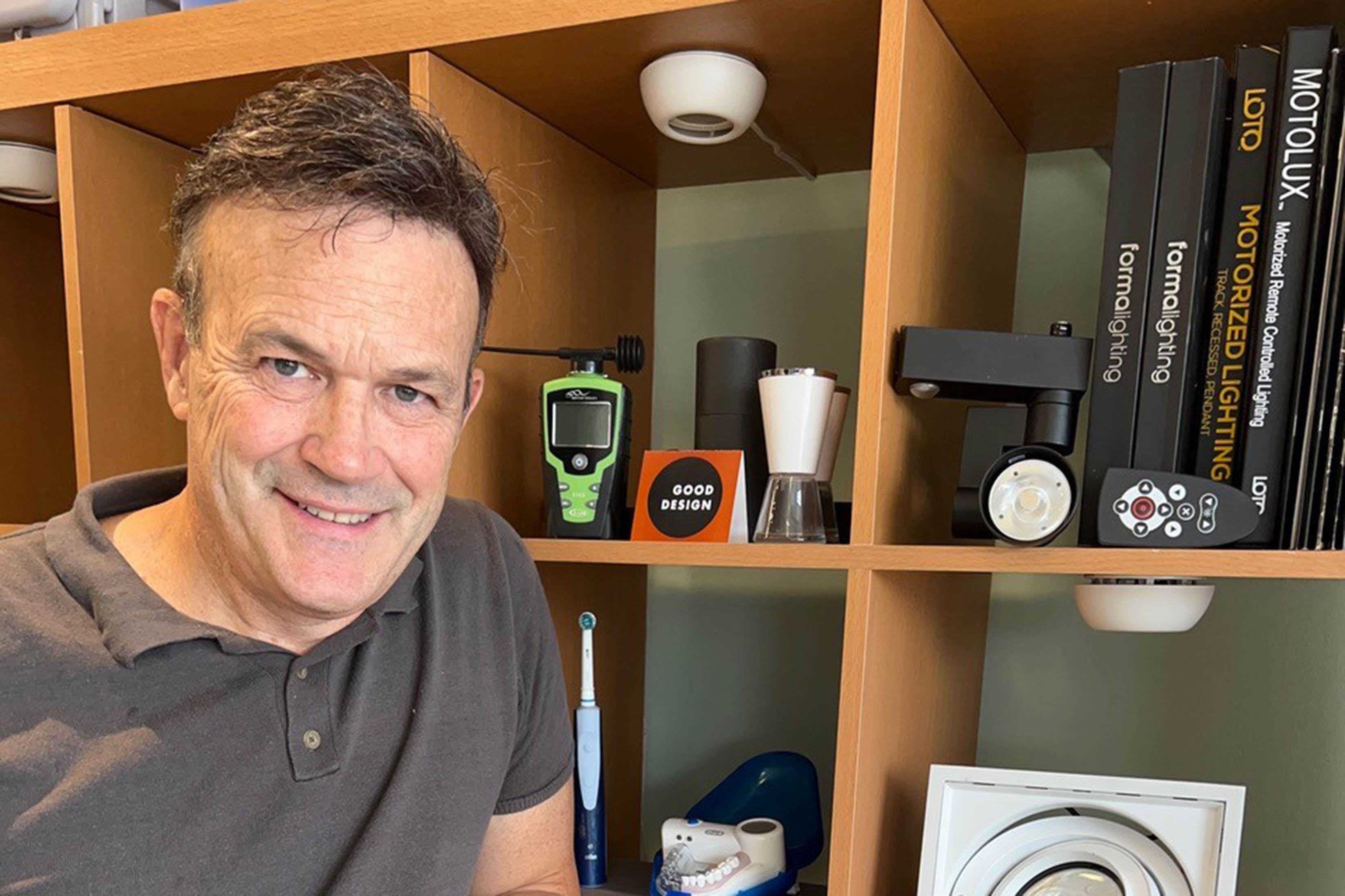 Tom Devlin poses (shoulders-up shot) in front of shelves featuring gadgets and a few books