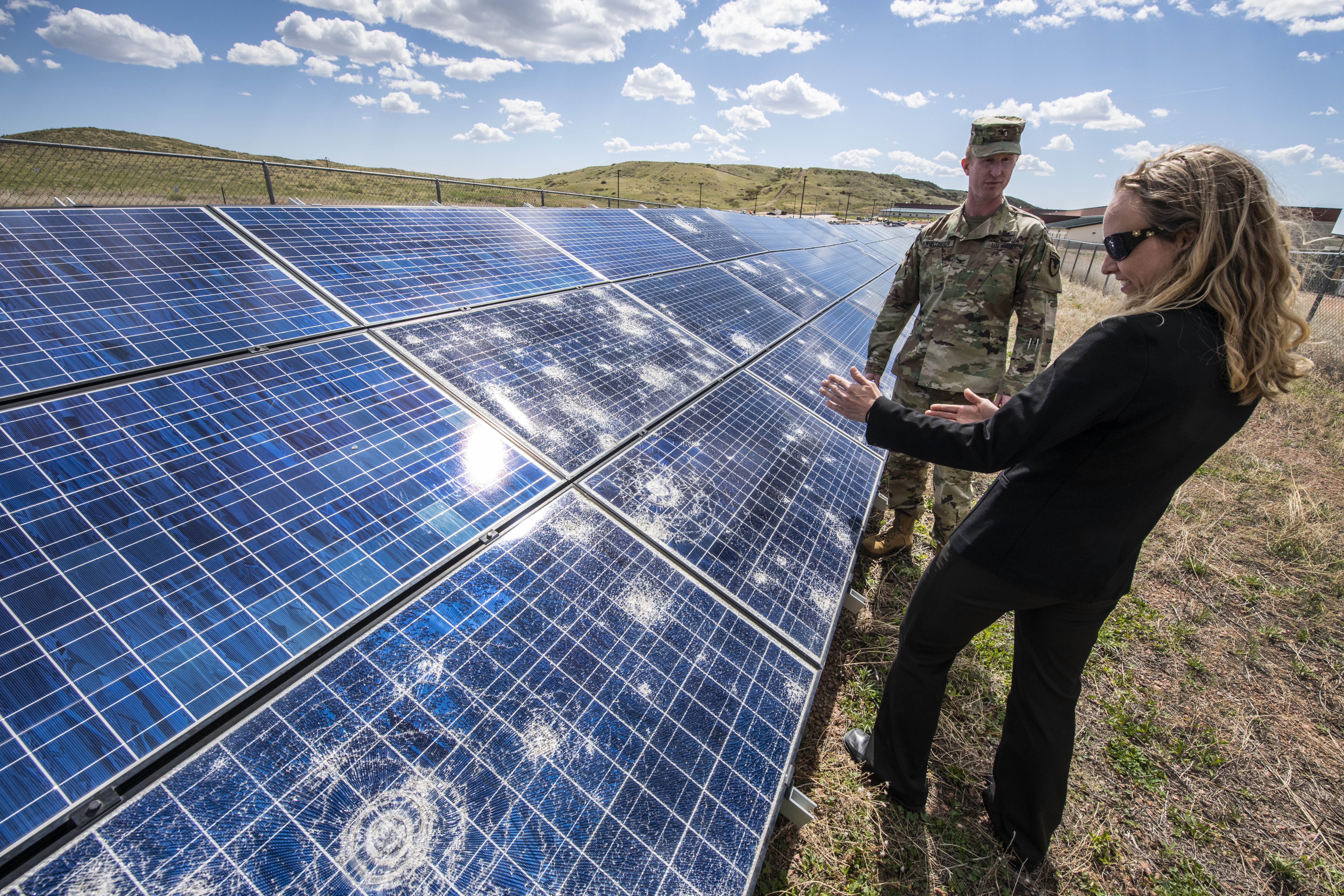 Kate Anderson and a man in uniform stand by a large solar array outside on a clear day.