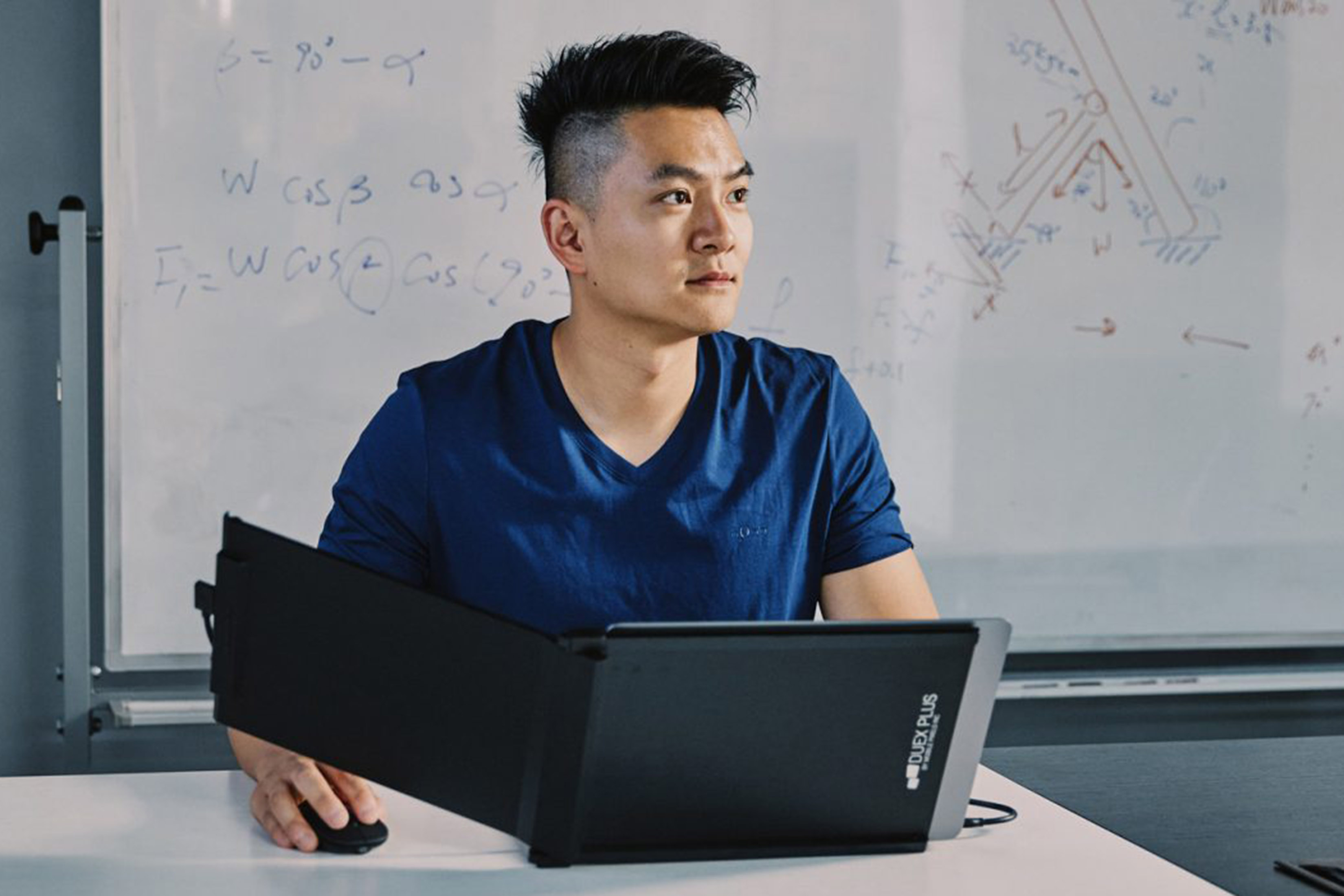 Jack Yao is shown at a table with a small computer screen in front of him. It has an extended display. A whiteboard is behind him.