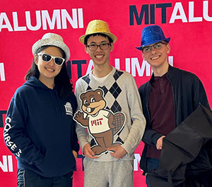 Students in hats and holding a Tim the Beaver cutout pose in front of a wall marked MIT Alumni.