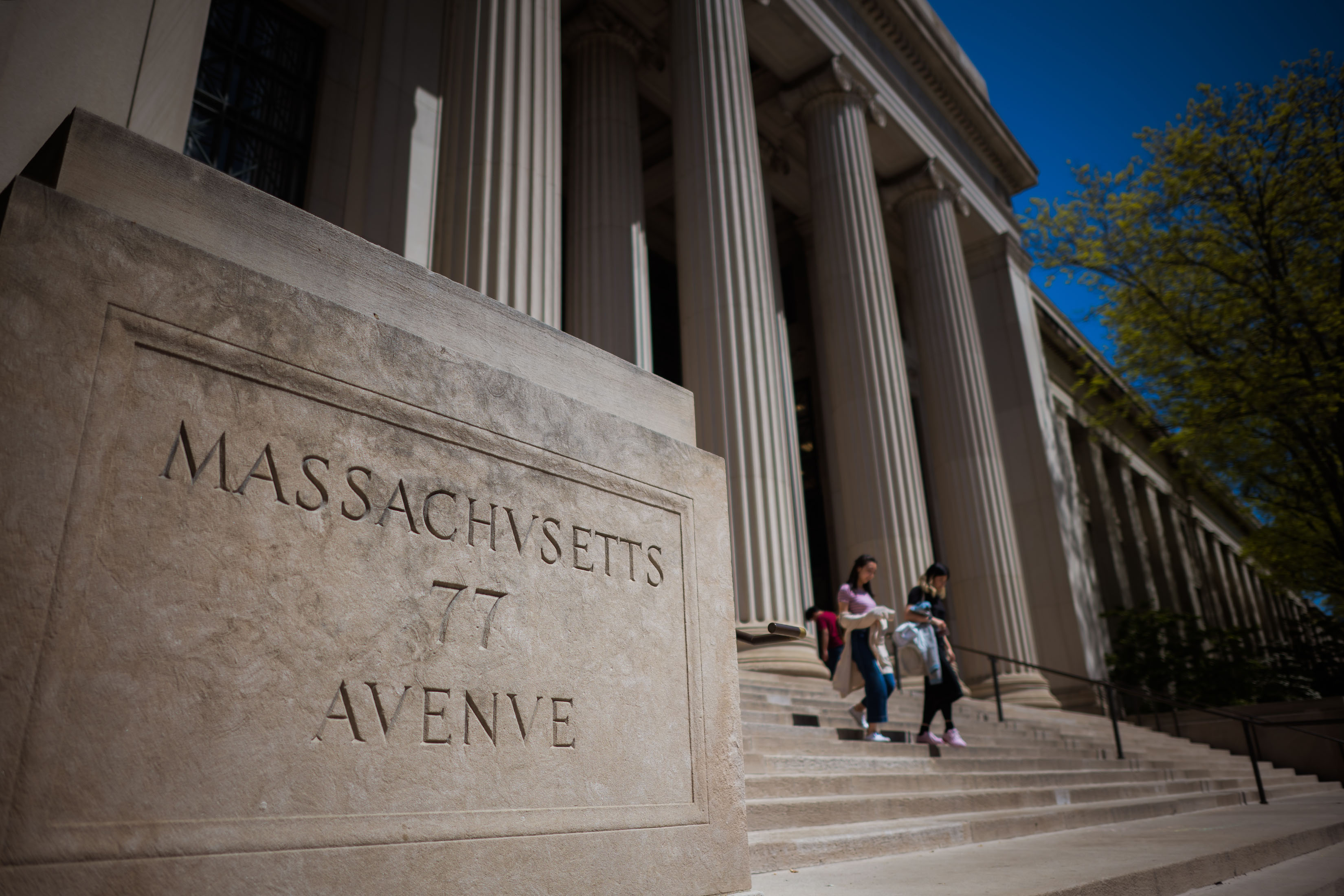 An angled view of MIT's 77 Mass Ave building showing the address carved in stone in foreground and columns in background