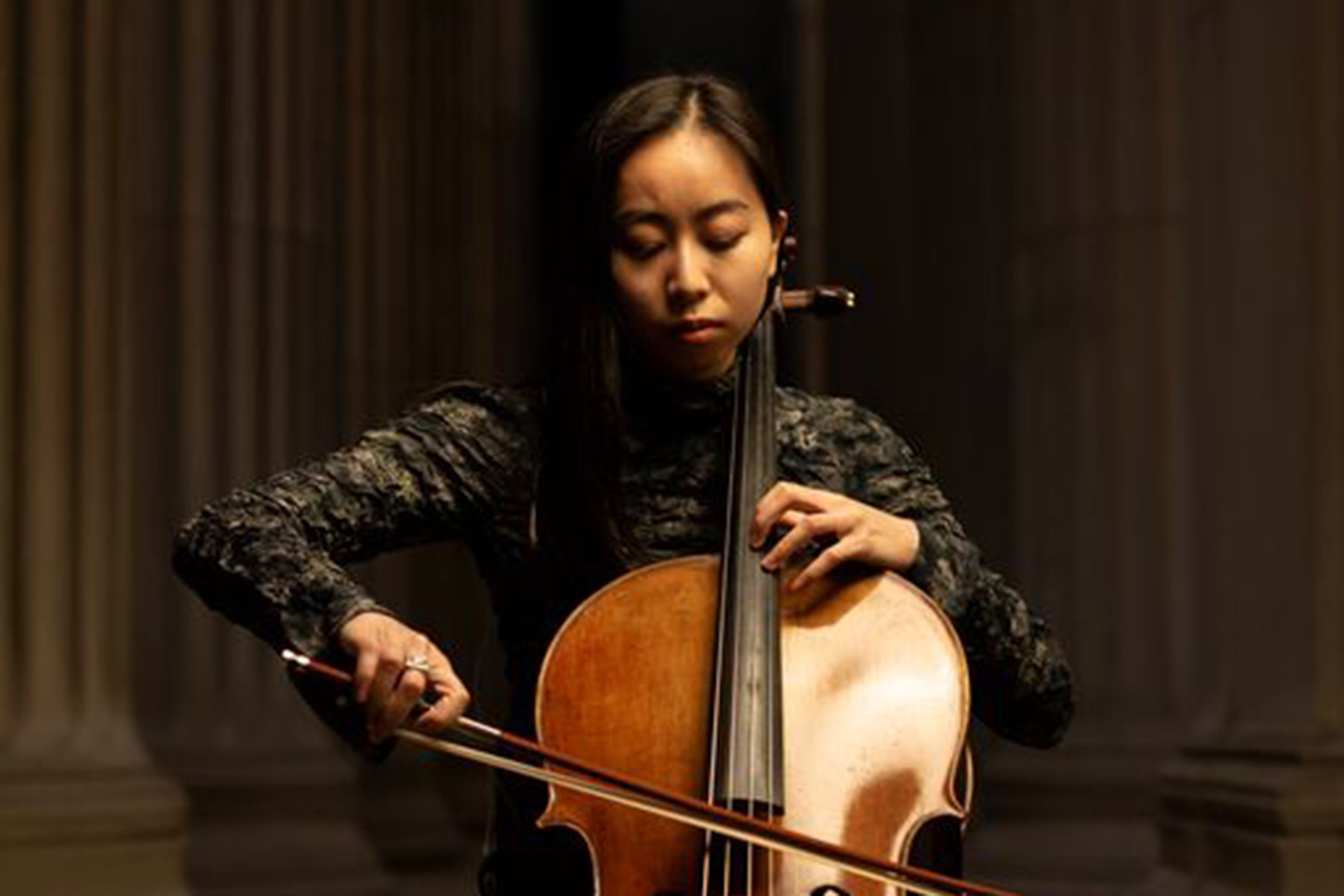 Valerie Chen is shown playing the cello. View is from mid-instrument up, and background is dark.