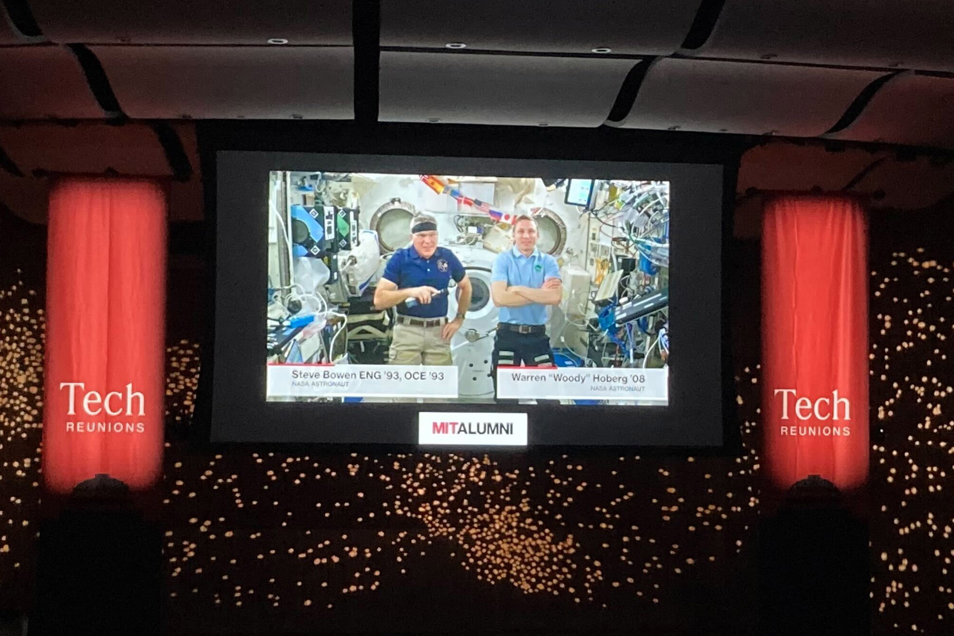 Astronauts Stephen Bowen ’93 and Warren “Woody” Hoburg ’08 are shown onscreen with Tech Day banners on either side.