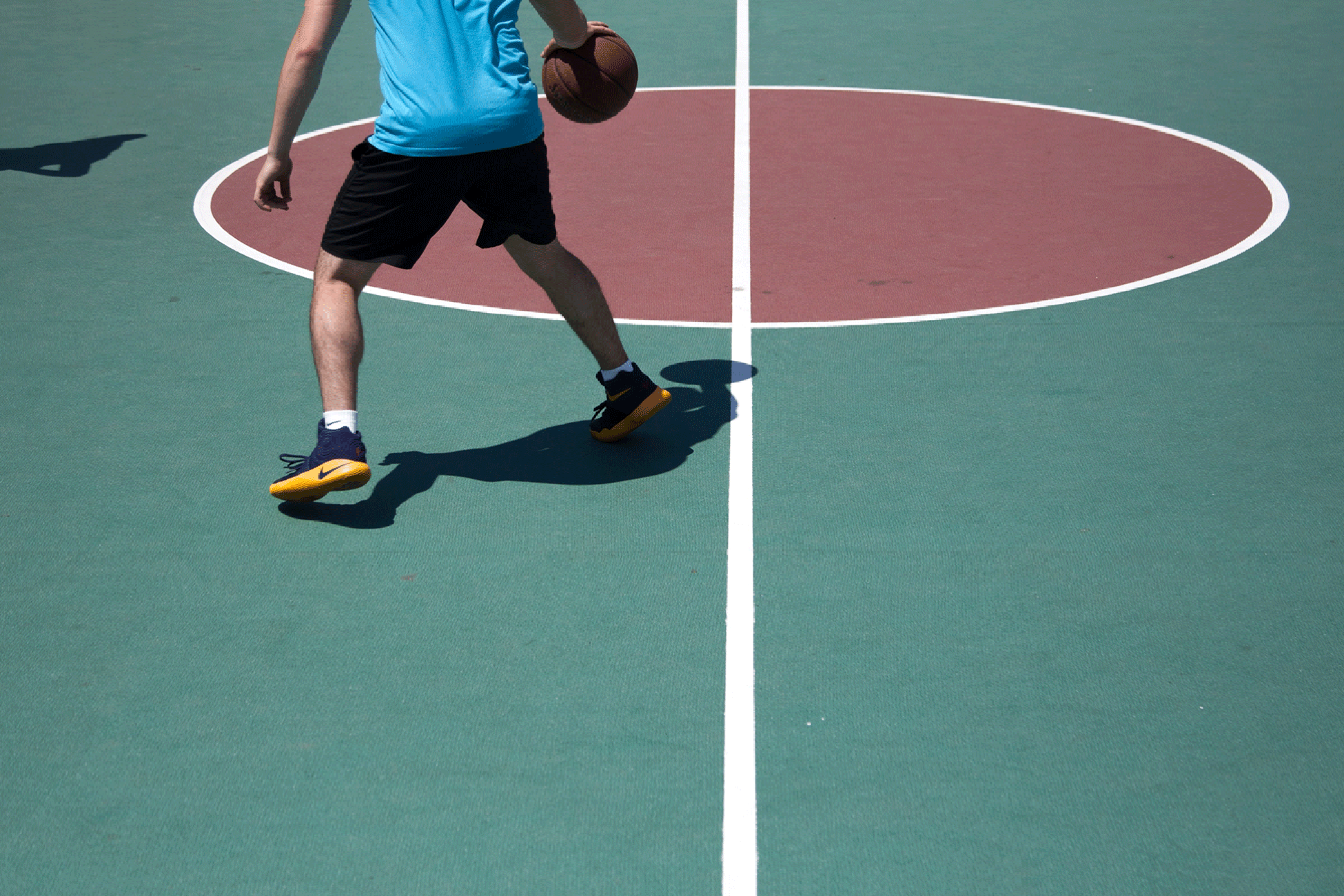 A basketball player is shown from the midriff down on a green court with a red circle.