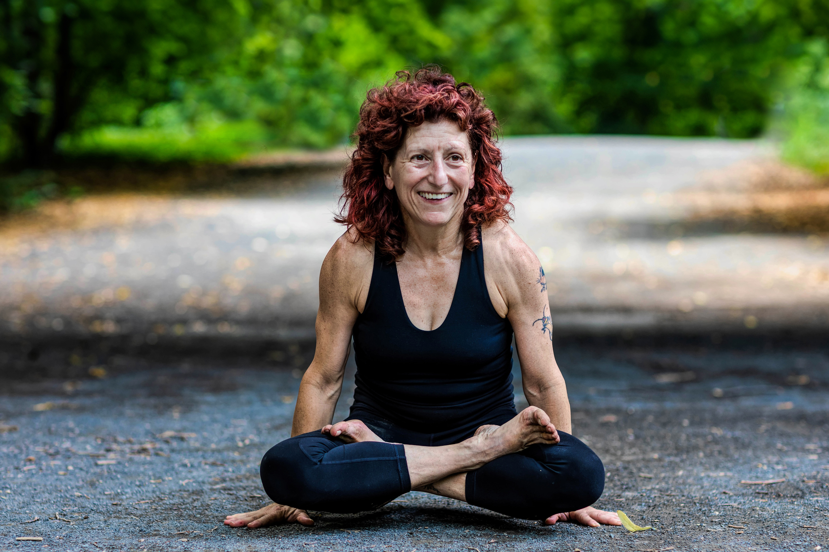 A photo of MIT alum Lillian Cuthbert in a crosslegged pose elevating her legs above pavement with trees behind her