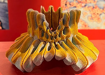 A copper carbonate sculpture is shown on display in the exhibition. It is a yellow abstract shape reminiscent of vertebrae.