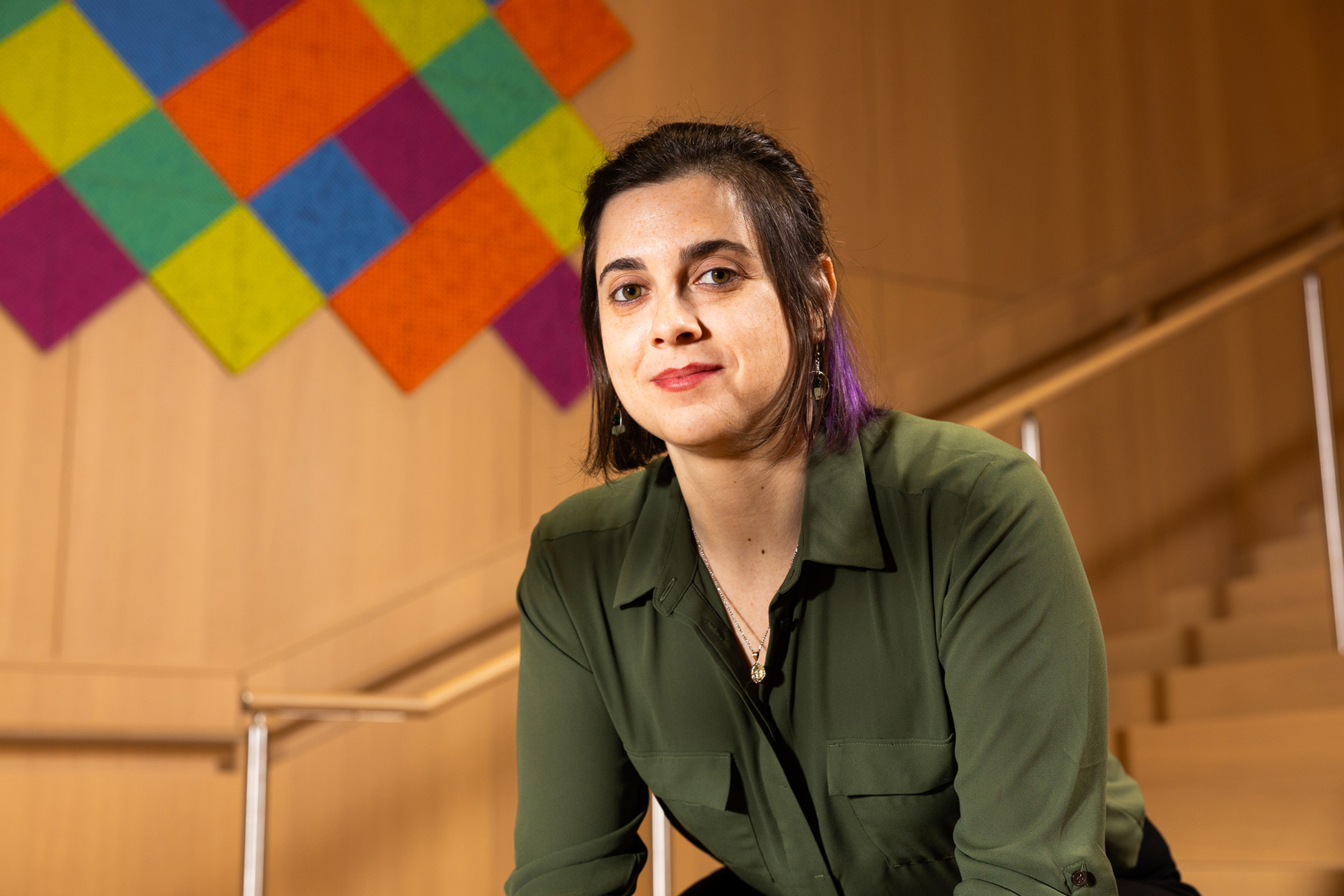 Portrait of Michelle Spektor PhD ’23 from waist up. A stairway railing is visible behind her as is a wooden wall with artwork made of blocks of color.