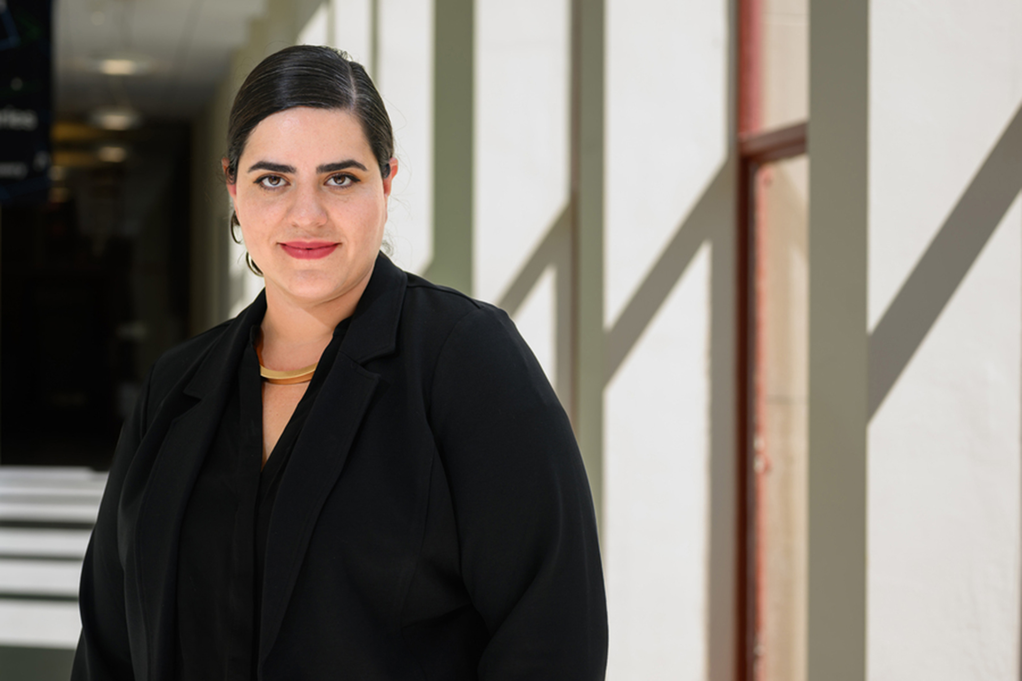 Portrait of Mariel García-Montes standing in a hallway. Shadows plan on the wall behind her.