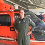 Eugene McGuiness stands in front of an orange aircraft carrier
