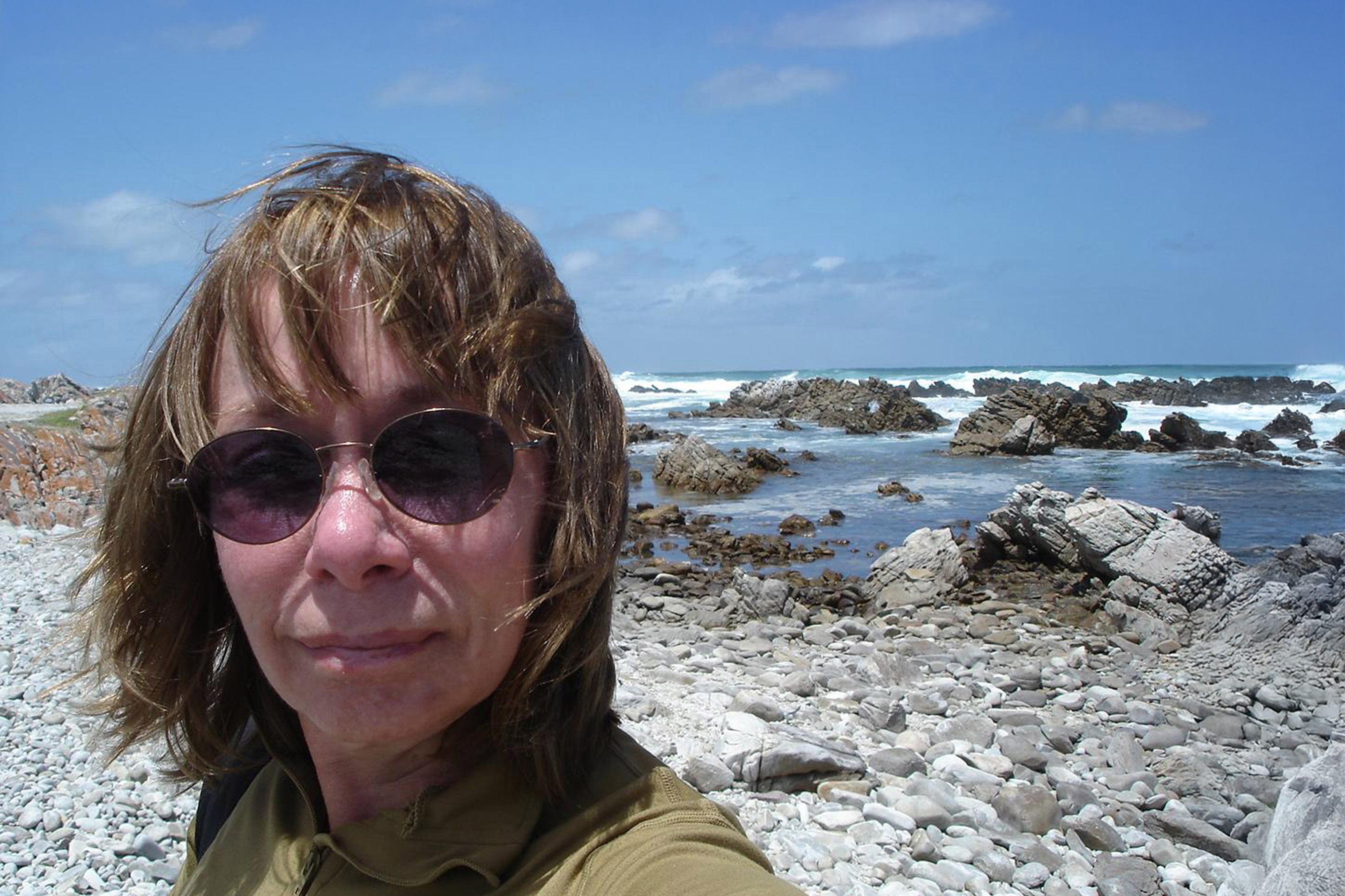 Darleen Ketten is shown in closeup, wearing sunglasses. A beach scene is behind her.