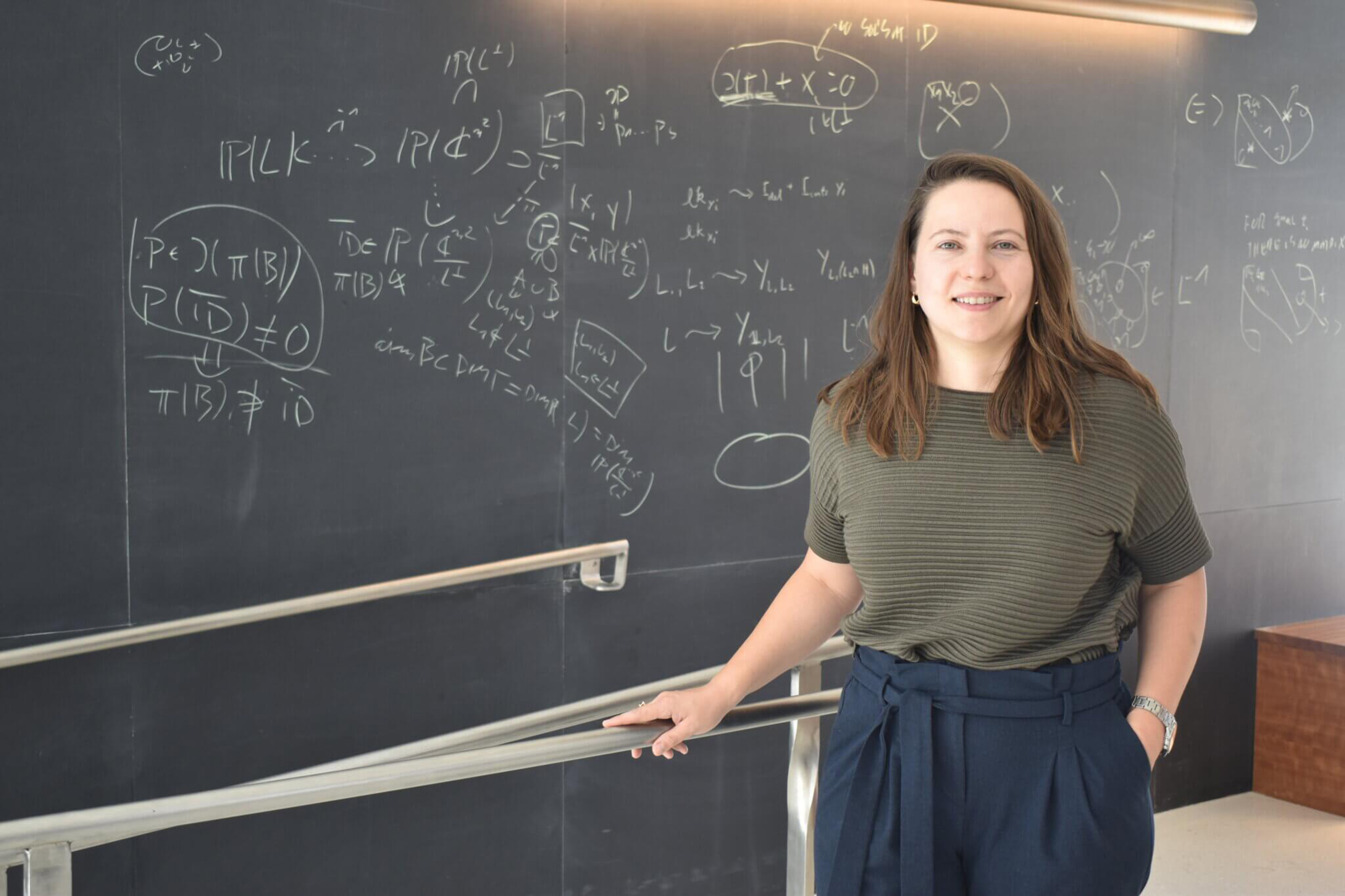 Alex Reiss-Sorokin stands in front of a blackboard full of equations.