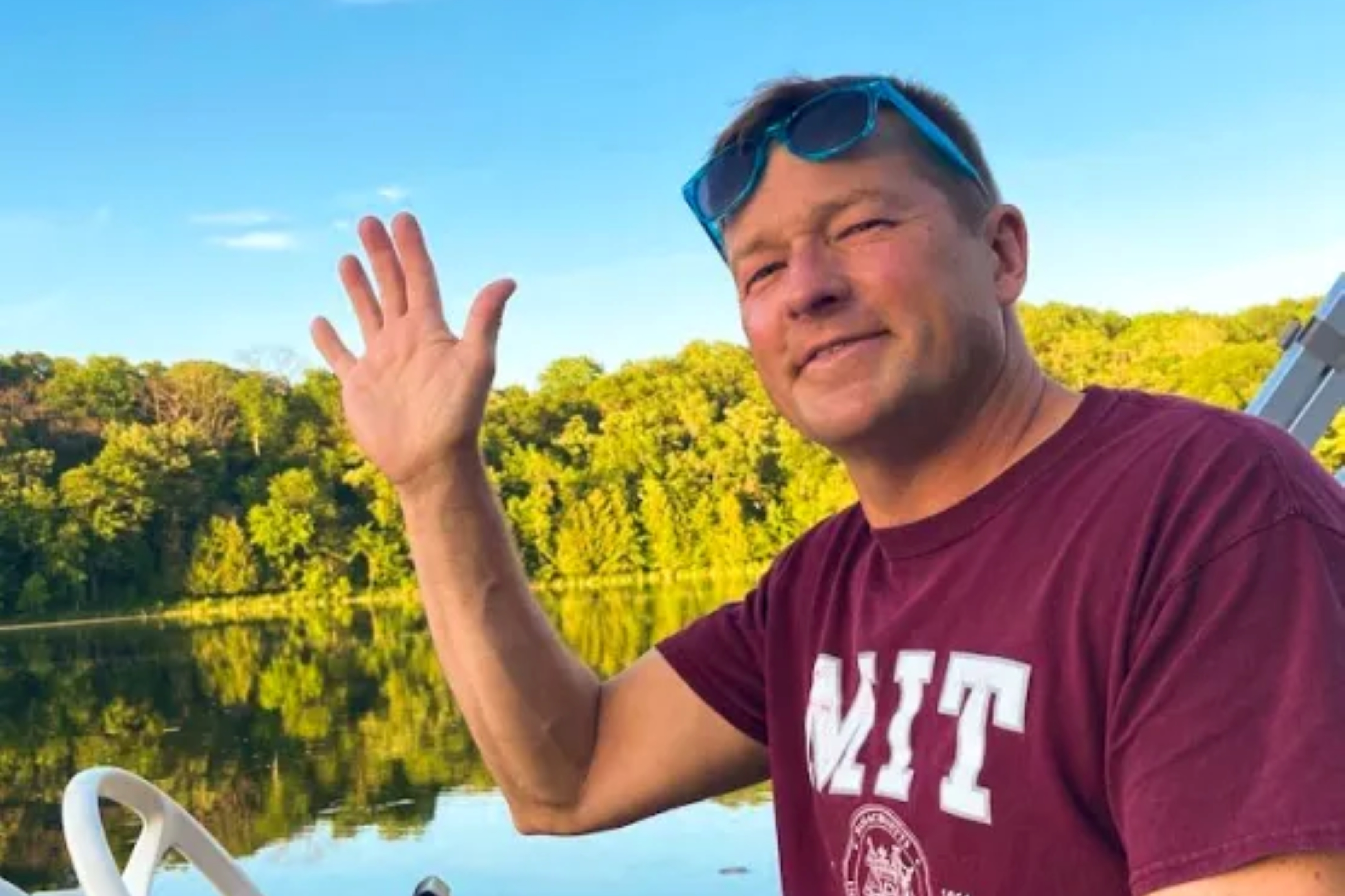Headshot of Andy Obst ’90 waving while on a boat, sunglasses perched on his head. He's wearing an MIT t-shirt