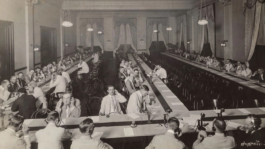 Black and white photo of 1500 alumni gathered in Symphony Hall for the 1916 transcontinental telephone circuit. Alumni are pictured seated at long tables answering telephones
