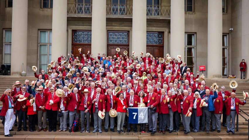 Photo of the 2024 Cardinal & Gray Society celebrating their 50th Reunion at Killian Court. Alumni wear their red jackets and gray scarves, smile, and some toss hats into the air