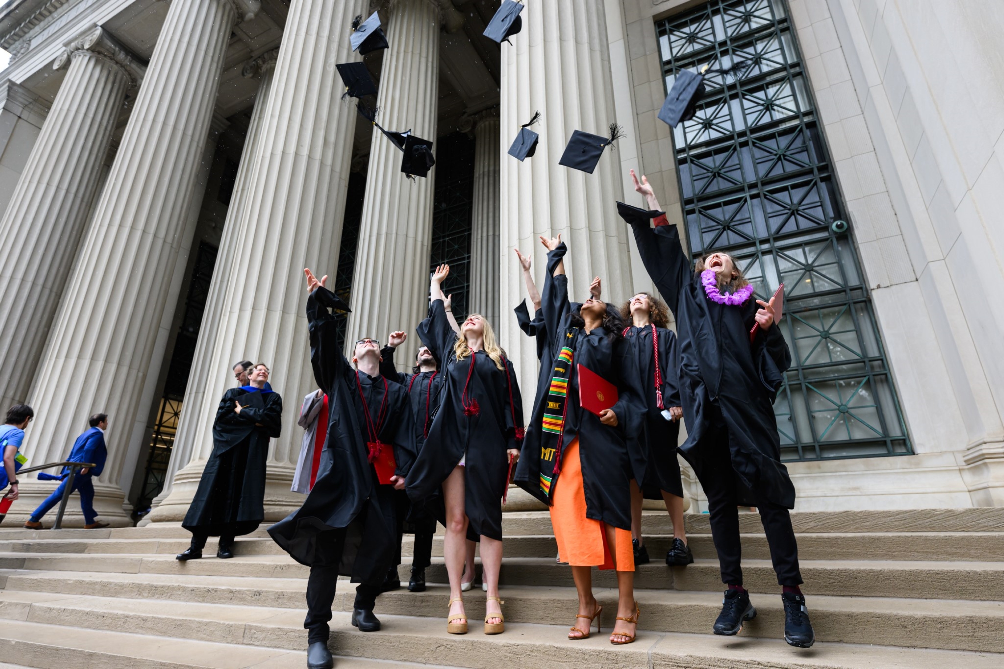 A group of graduates toss their caps into the air on the steps of Killian court