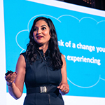 A photo of MIT alum Parul Somani giving a presentation with a blue image behind her