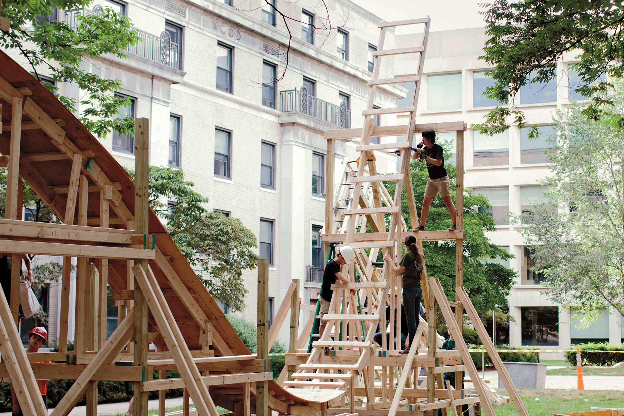 A photo of a wooden roller coaster structure outside in a courtyard with building surrounding it