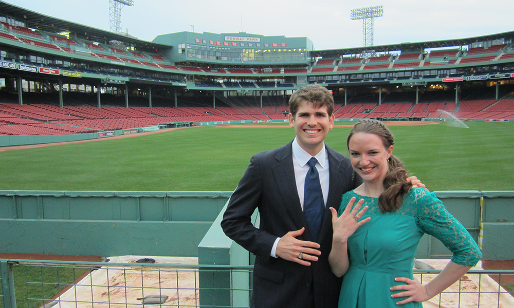 Nicole Gagnier and Alex Klein standing in Fenway Park with the outfield behind them showing their Brass Rats 