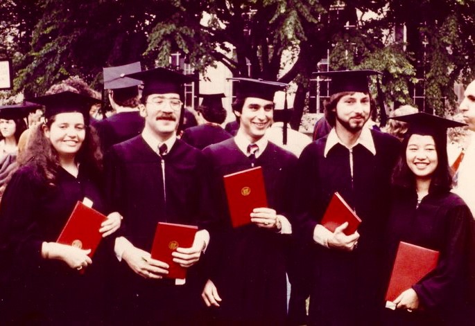 Five people holding diplomas and wearing graduation robes on Killian court 