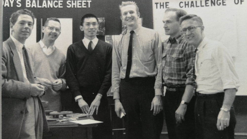 Black and white photo of students at MIT in 1957 by a table with an architectural model