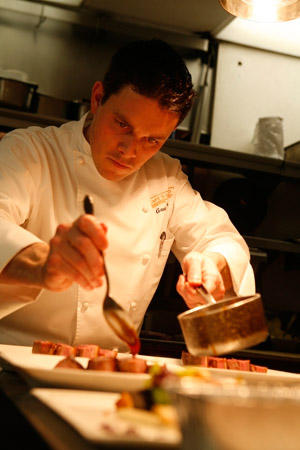 Chef Gavin Kaysen sauces a dish of Magret de Canard at Cafe Boulud in New York. (© Owen Franken).