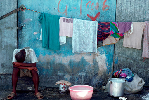 A man sits with his head bowed in an impoverished neighborhood of Port au Prince, Haiti, July 1984 (© Owen Franken).