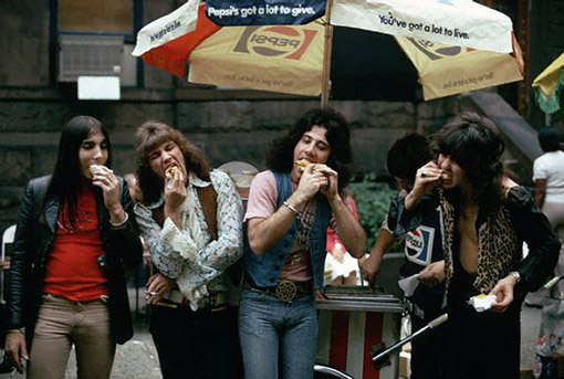 Four men enjoy hot dogs by a New York hot dog stand, October 1973