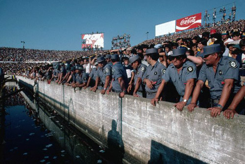 Police at a soccer game in Buenos Aires, Argentina, line a moat filled with water to prevent fans from crashing the field, March 1981 (© Owen Franken/CORBIS).