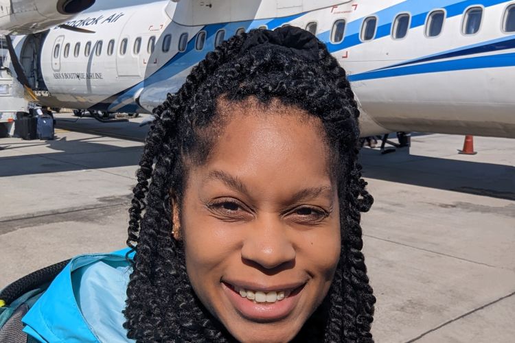 Jamila Smith-Dell taking a selfie on a tarmac with a plane behind her