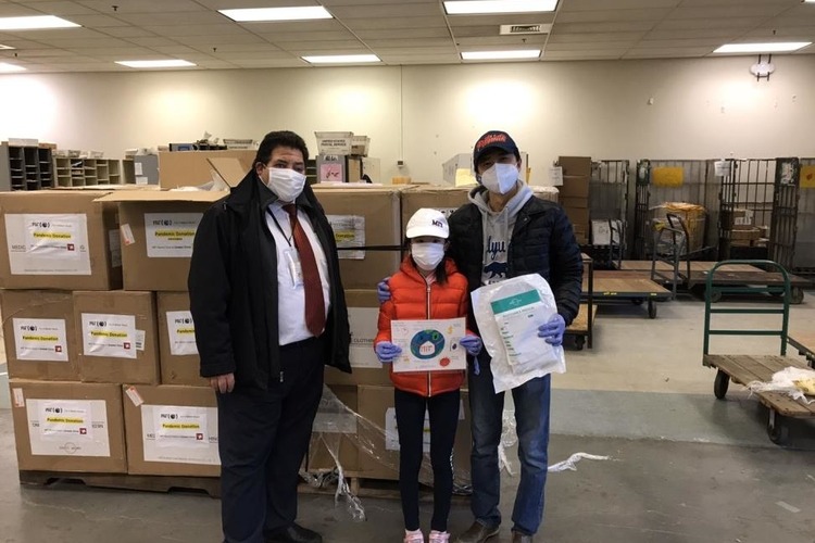 Three people with masks on standing in front of boxes
