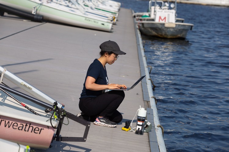 Woman in a hat kneeling on a boat launch with a laptop